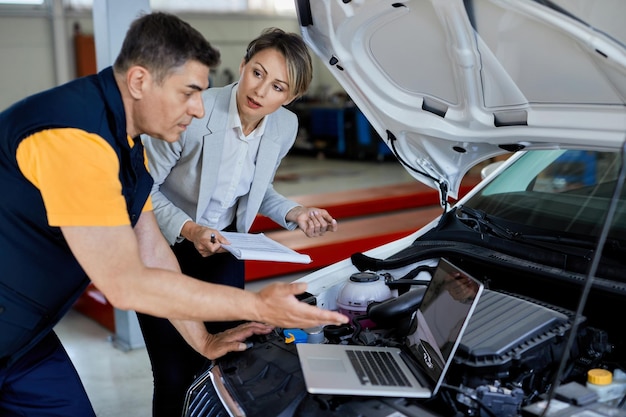 Female manager and car mechanic cooperating while using laptop and testing engine performance in auto repair shop