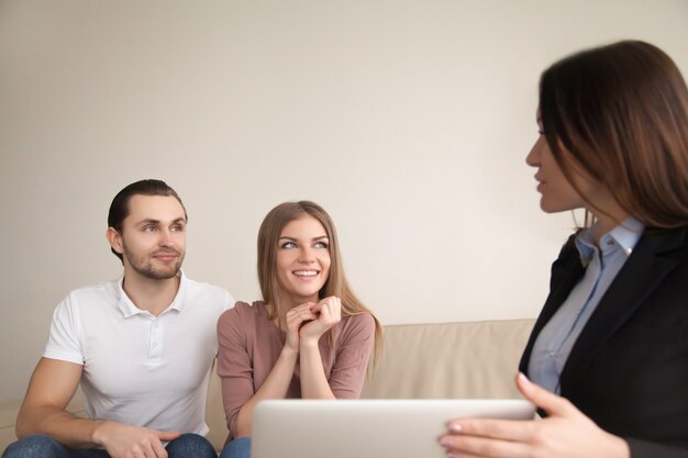 Female manager or realtor talking to young happy couple indoors