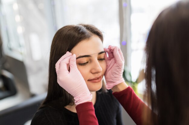 Female master checks the contour of the eyebrows with thread