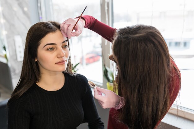 Female master put eyebrow paint with brush during make-up procedure