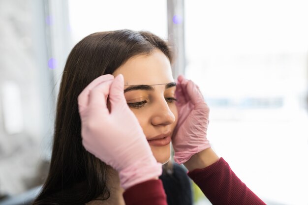 白い手袋をした女性マスターが眉毛の輪郭を糸でチェック