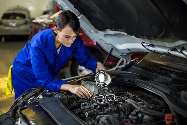 Female mechanic examining a car engine with lamp