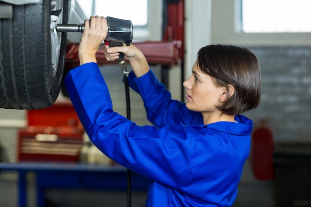 Free photo female mechanic fixing a car wheel with pneumatic wrench