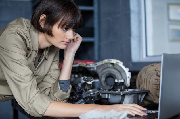 Free photo female mechanic leaning on table and using laptop