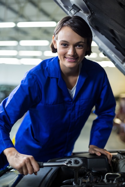 Meccanico femminile sorridente, mentre la manutenzione di un auto