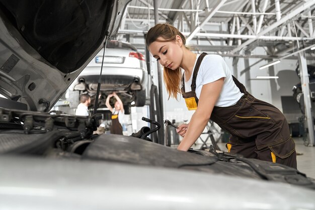 Female mechanic in white shirt and coverall repairing engine