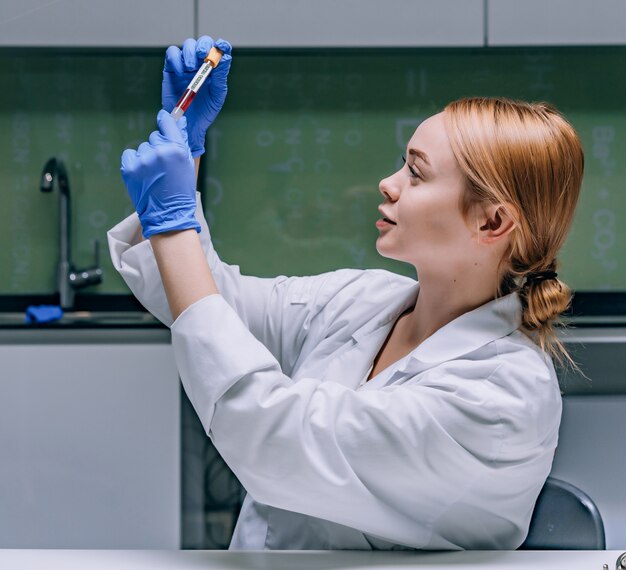 Female medical or scientific researcher looking at a test tube in a laboratory.