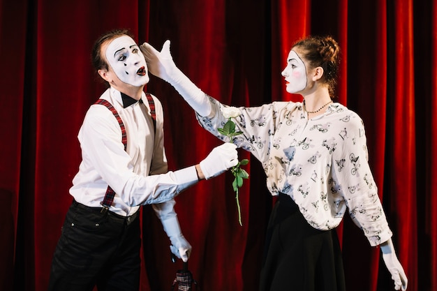 Free photo female mime artist giving slap to male mime holding white rose