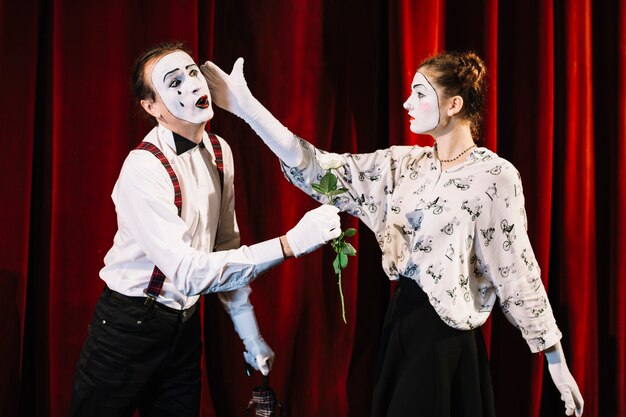 Female mime artist giving slap to male mime holding white rose