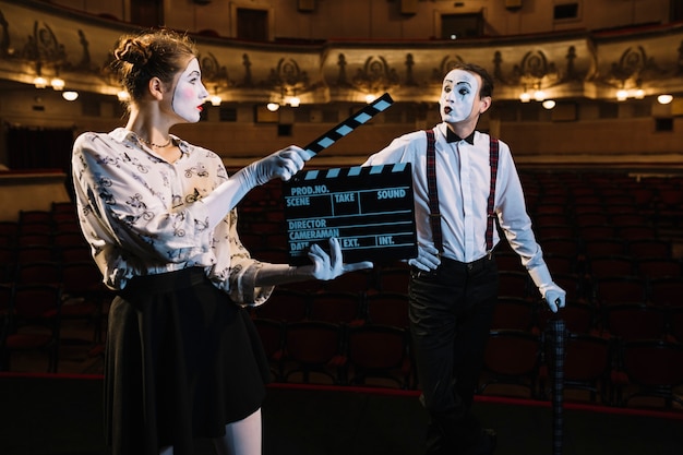 Female mime artist holding clapper in front of male mime artist performing on stage