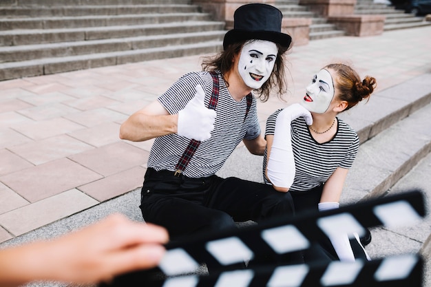 Female mime looking at male mime gesturing thumbs up