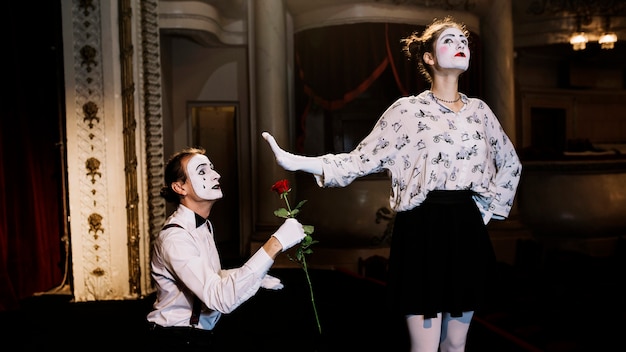 Female mime showing stop gesture to male mime artist holding red rose