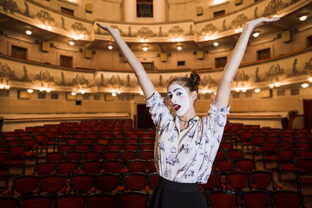 female mime standing in an auditorium raising her arms