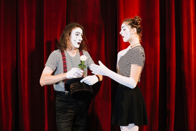 빨간 커튼 앞에 서있는 남성 mime에서 흰색 장미를 복용 여성 mime