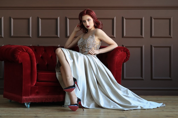 Female model in blue elegant gown sitting on the red sofa