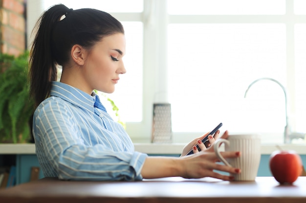 Modello femminile in camicia blu, giocando con il suo telefono e avendo una tazza di bevanda