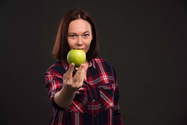 Foto gratuita modello femminile in abiti da collezione autunno inverno che tiene una mela verde e guarda con appetito.