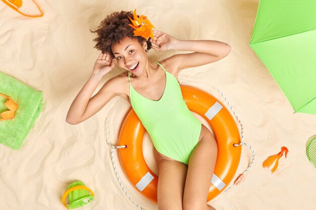 female model in green bikini poses on inflated lifebuoy keeps hands behind head enjoys summer vacation uses sunscreen lotion has happy mood during perfect holidays