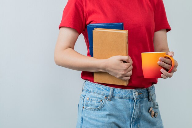 Женская модель в красной рубашке, держа книги и чашку напитка.