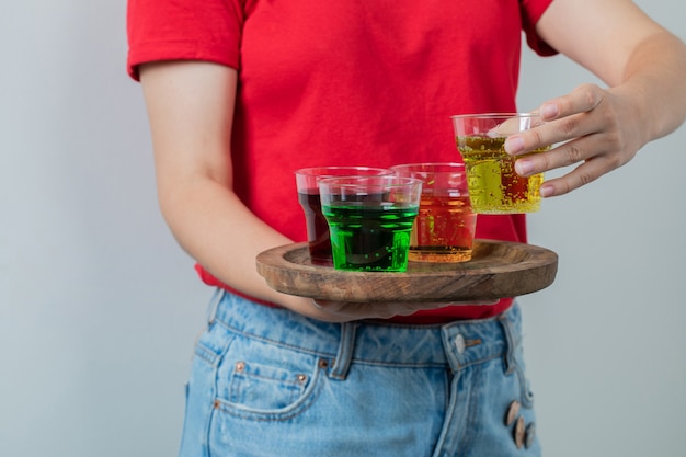 Female model in red shirt holding a platter of drinks. 