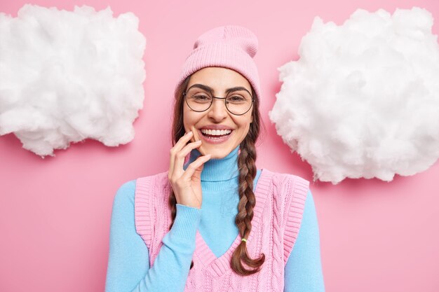 女性モデルの笑顔は幸せな感情を幅広く表現し、白い歯はピンクに隔離された透明な眼鏡の丸いカジュアルな服を着ている