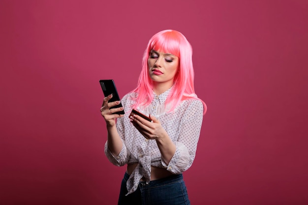 온라인 쇼핑 의류 구매를 위해 신용카드나 직불카드와 스마트폰을 사용하는 분홍색 머리를 한 여성 모델. 휴대폰 소매 앱을 사용하여 인터넷 웹사이트에서 구매하기 위해 돈 거래를 합니다.
