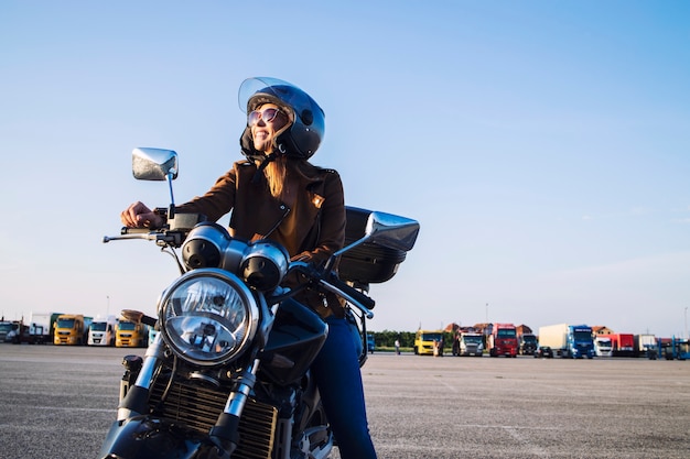 가죽 재킷과 헬멧 복고풍 오토바이에 앉아 웃 고있는 여성 오토바이