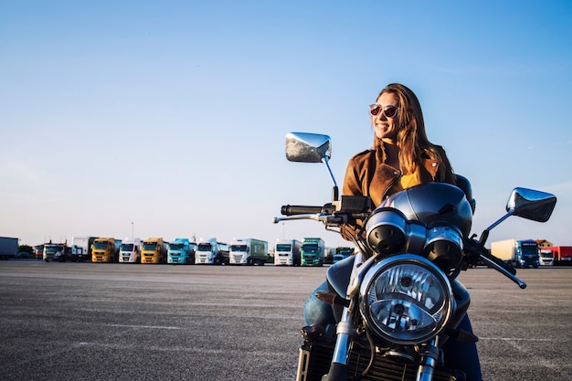 Female motorcyclist in leather jacket sitting on retro motorbike and smiling