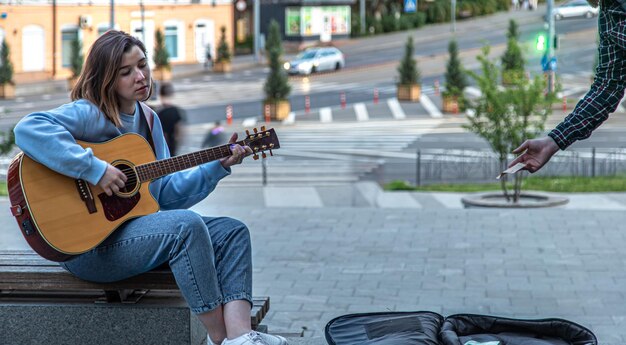 Женщина-музыкант играет на акустической гитаре и поет на улице на улице