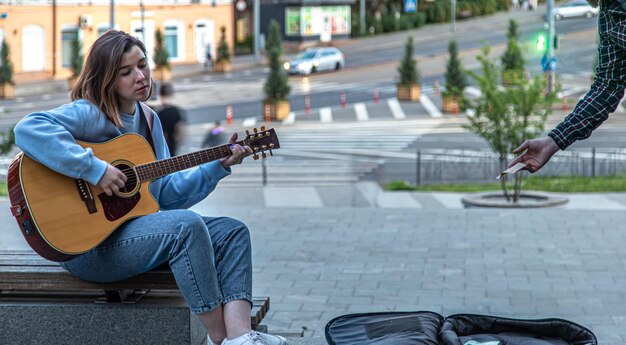 Female musician busking playing acoustic guitar and singing outdoors in street