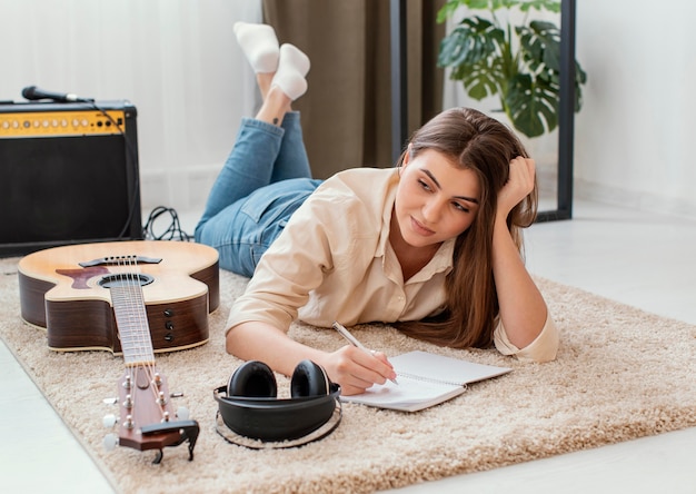 Female musician at home writing song with headphones and acoustic guitar
