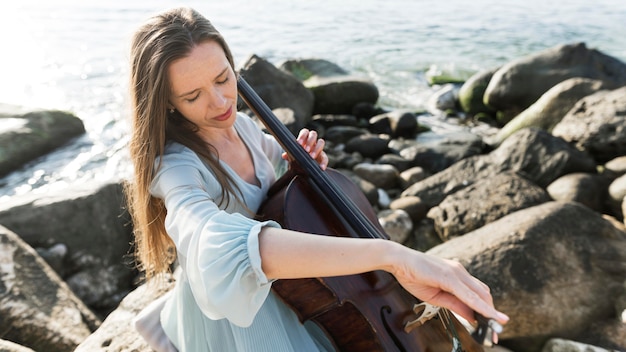 Женский музыкант играет на виолончели у океана
