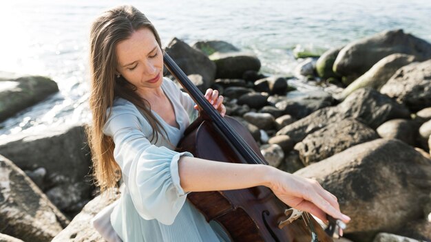 Female musician playing cello by the ocean