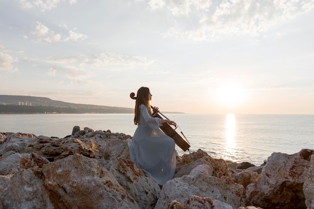 Musicista femminile che suona il violoncello all'aperto al tramonto