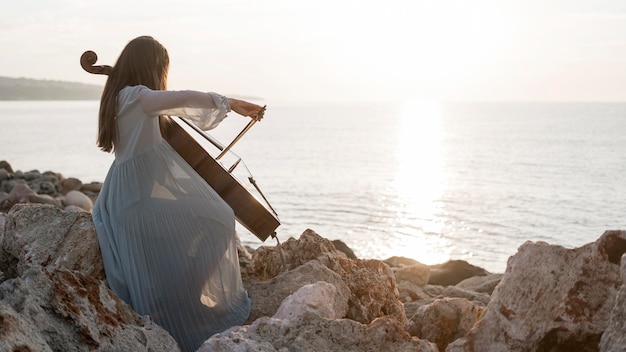 Female musician playing cello at sunset on rocks with copy space