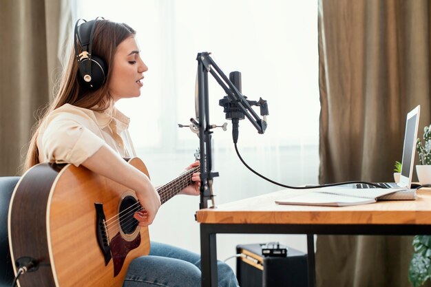 Female musician recording song at home while playing acoustic guitar