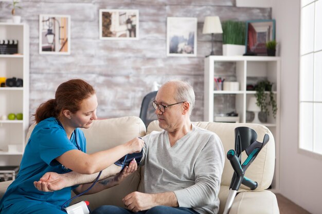 血圧をチェックするために老人の腕にデジタルデバイスを取り付けている女性看護師。