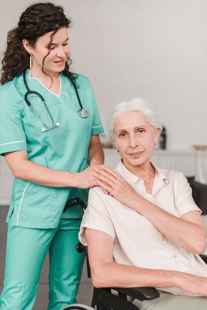 Female nurse giving support to senior woman sitting on wheel chair