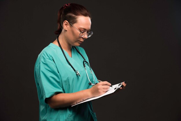 Female nurse in green uniform holding the blank and taking notes. 