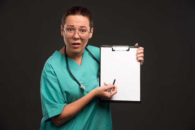 緑の制服を着た女性看護師は、患者の病歴を示し、質問をします。