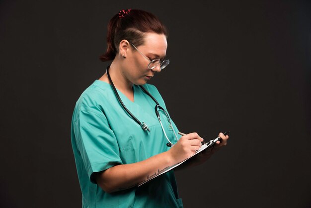 Female nurse in green uniform takes notes.