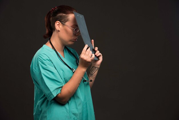 Female nurse in green uniform takes notes.