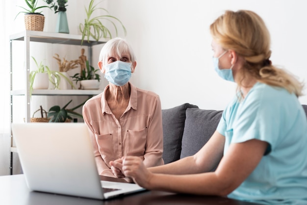 Female nurse and older woman conversing over laptop at nursing home