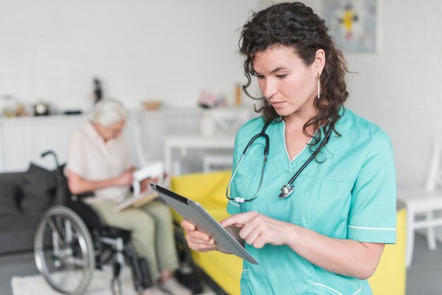 Female nurse using digital tablet standing in front of senior woman sitting on wheelchair