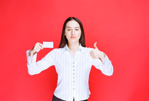 Female office employee showing business card and giving thumbs up. 