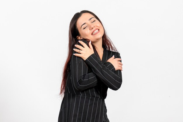 female office employee in strict black suit hugging herself on white