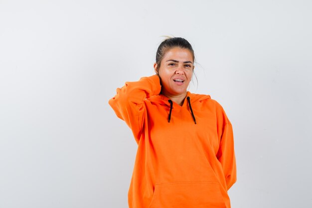 Female in orange hoodie holding hand on neck and looking charming 