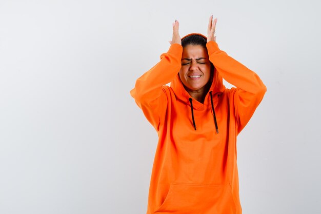 Female in orange hoodie holding hands on head and looking regretful 