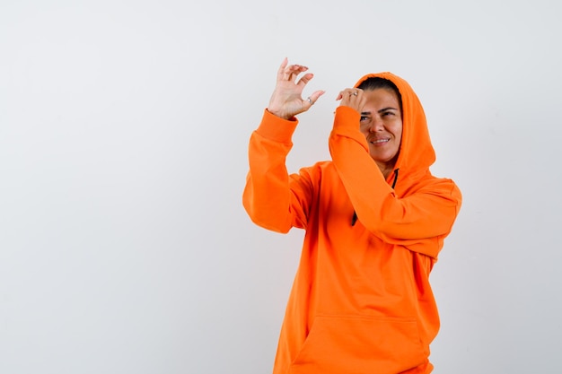 Female in orange hoodie pretending to hold telescope and looking confident 
