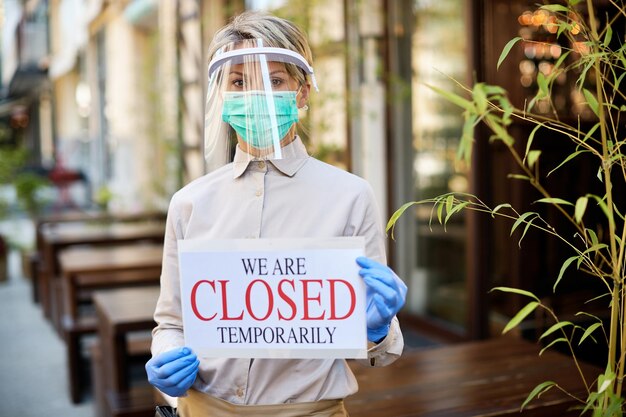 코로나바이러스 전염병으로 인해 야외 카페에서 닫힌 표지판을 들고 있는 여성 소유자